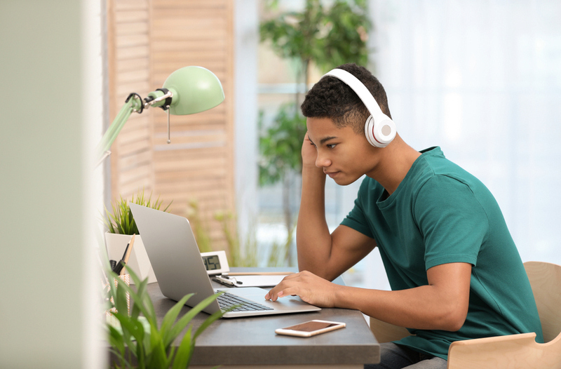 African-american,Teenage,Boy,With,Headphones,Using,Laptop,At,Table,In